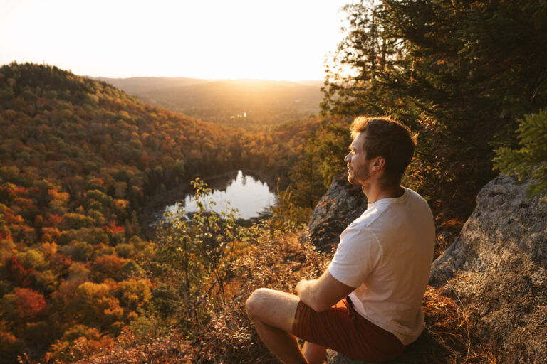 man sitting on a summit at sunset surrounded by fall colors
